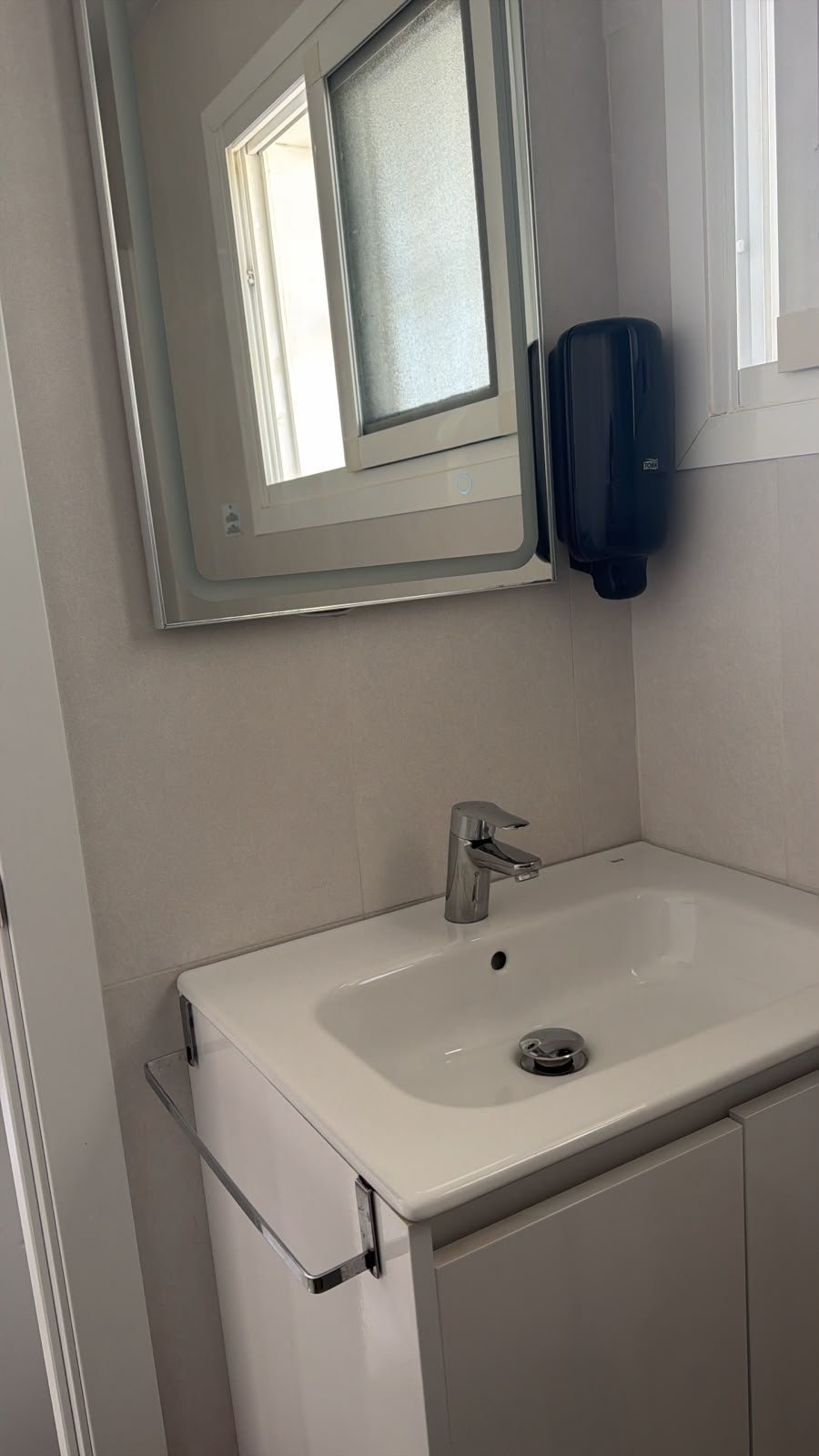 Modern bathroom sink with chrome faucet, mirror above, and black soap dispenser on beige wall