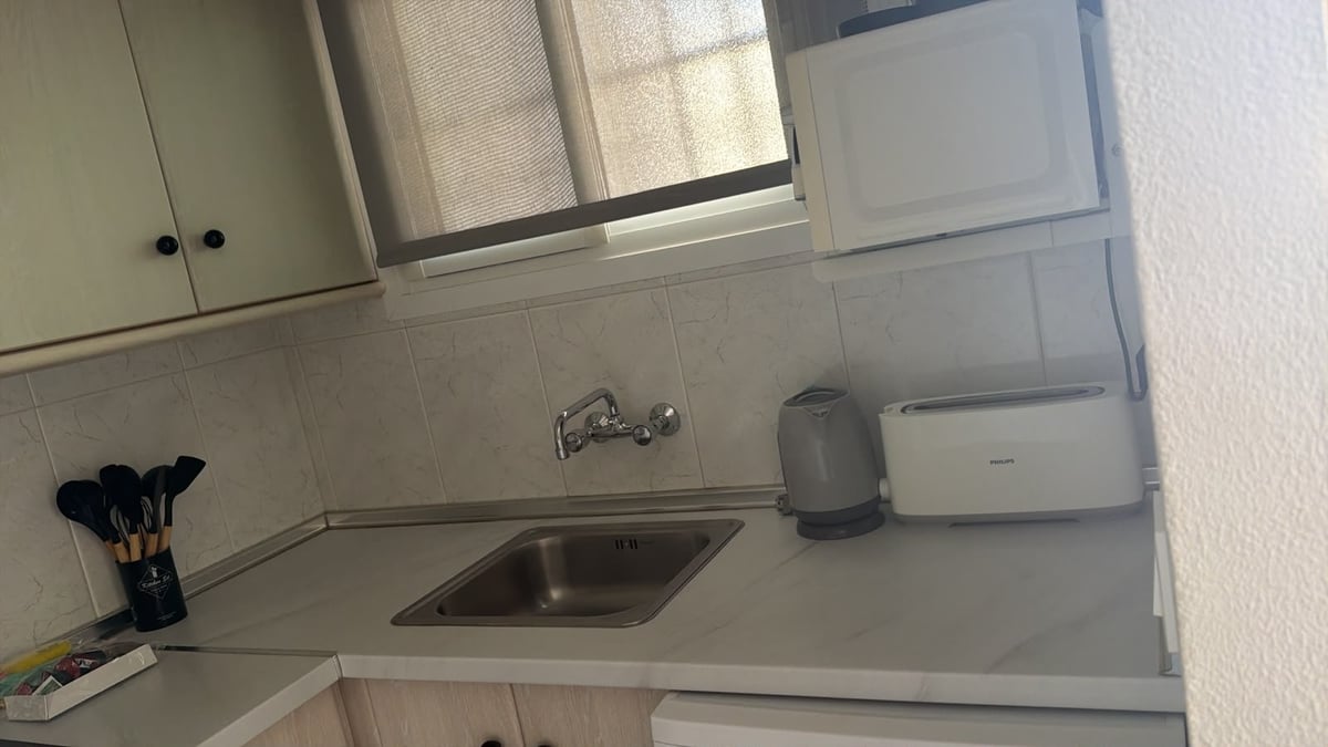 Compact kitchen sink with stainless steel basin, white countertop, wall-mounted faucet, and cabinets above