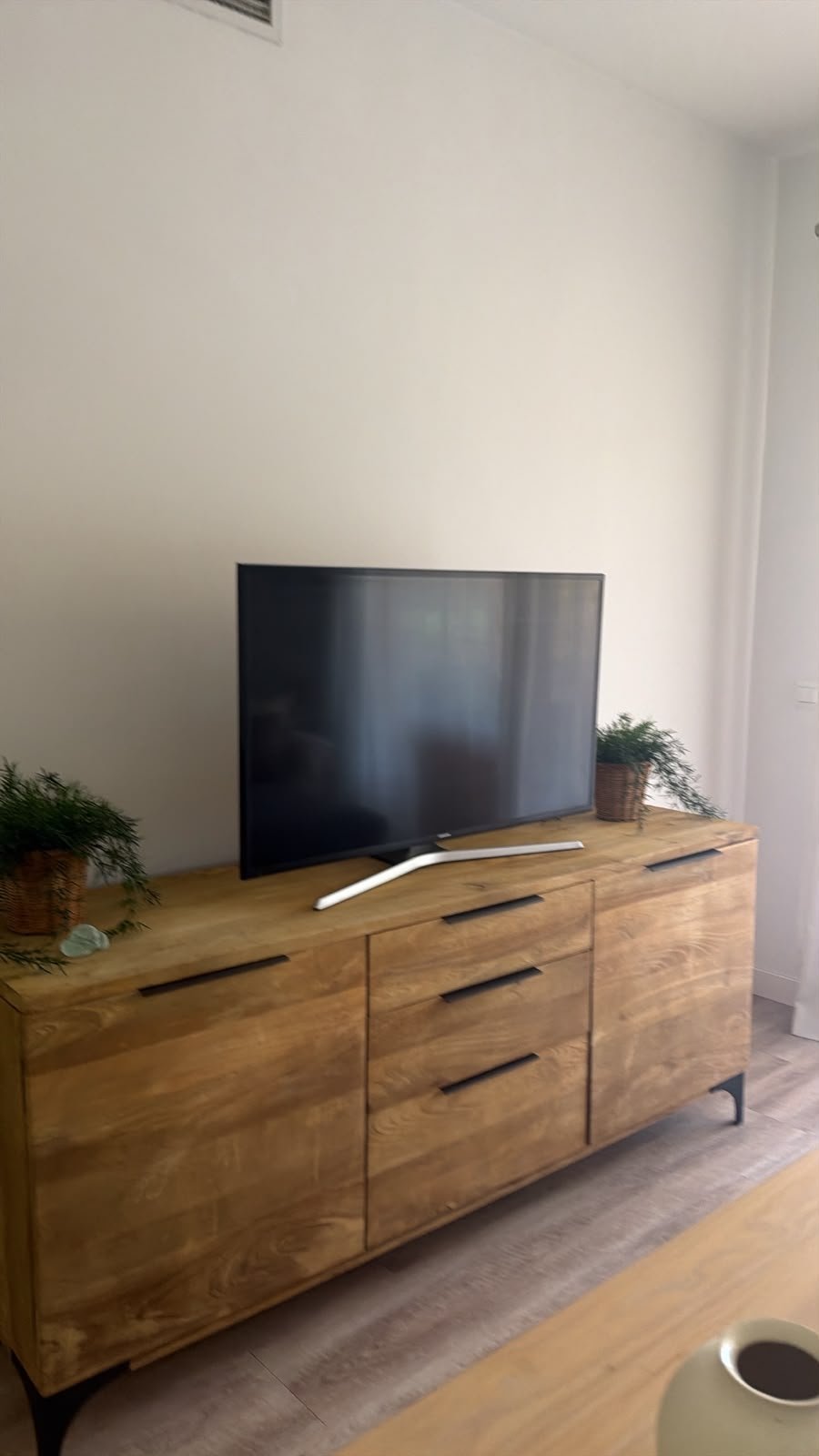Wooden TV console with a flat-screen television and potted plant in a modern living room with white walls